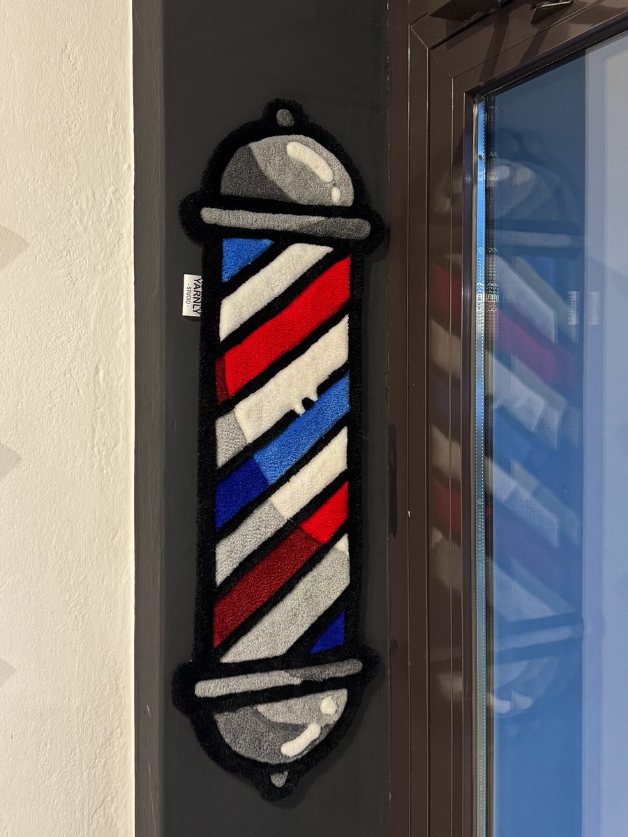 Ręcznie tuftowany dywan w kształcie słupa fryzjerskiego, zawieszony przy wejściu do barbershopu
